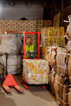 Foto de Un trabajador que usa un apilador levanta y transporta una caja de cartón de carga con cosas para reciclar en una estación de basura - Imagen libre de derechos