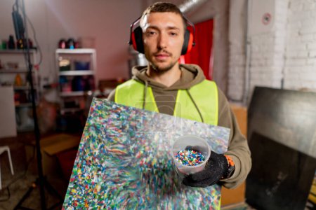 Photo for A factory employee holds a painting made from shredded plastic bottle caps at a waste recycling station - Royalty Free Image
