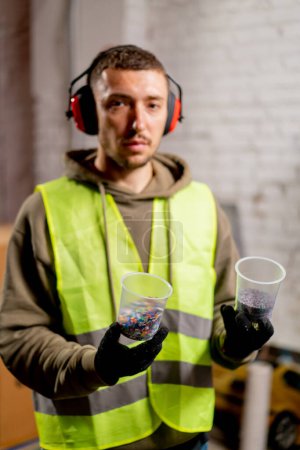 Foto de Retrato de un hombre en uniforme y auriculares con gafas con tapas de plástico triturado para reciclar - Imagen libre de derechos