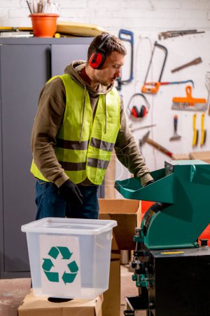 Photo for A waste recycling station employee wearing noise-canceling headphones turns on a special machine for shredding used plastic caps - Royalty Free Image