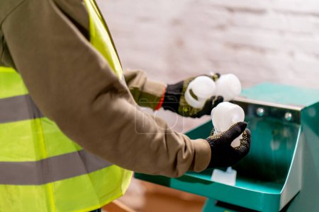 Photo for Close-up shot of male hands in gloves pouring plastic caps into a shredding apparatus for recycling - Royalty Free Image