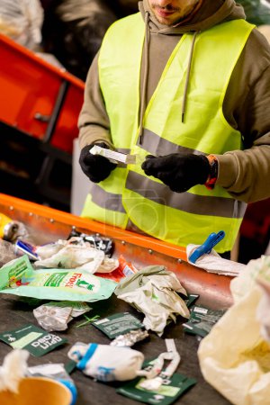 Foto de Las manos en los guantes de un empleado uniformado clasifican la basura en categorías en una línea especial en una planta de reciclaje de residuos - Imagen libre de derechos