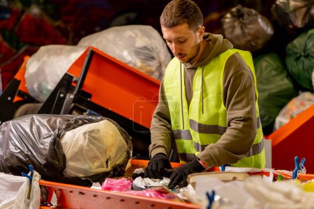 Téléchargez les photos : Vue latérale d'un homme en uniforme travaillant sur une ligne de distribution d'ordures et triant les déchets dans des conteneurs spéciaux - en image libre de droit