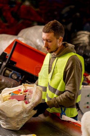 Photo for Side view of a man in uniform working on a garbage distribution line and sorting waste into special containers - Royalty Free Image
