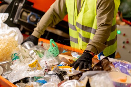 Foto de Las manos en los guantes de un empleado uniformado clasifican la basura en categorías en una línea especial en una planta de reciclaje de residuos - Imagen libre de derechos