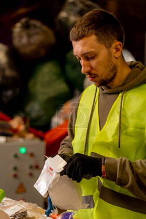 Foto de Vista lateral de un hombre de uniforme que trabaja en una línea de distribución de basura y clasifica los residuos en contenedores especiales - Imagen libre de derechos