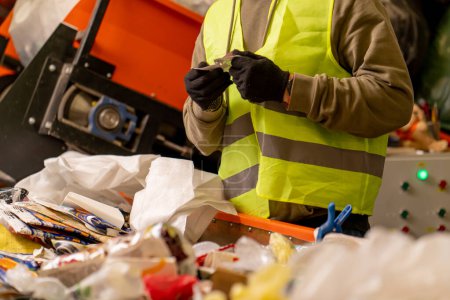 Téléchargez les photos : Mains dans les gants d'un employé en uniforme trier les déchets en catégories sur une ligne spéciale dans une usine de recyclage des déchets - en image libre de droit