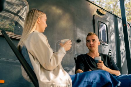 Téléchargez les photos : Un beau mec boit du thé sur la véranda près de la maison mobile et a une conversation fascinante avec sa petite amie - en image libre de droit