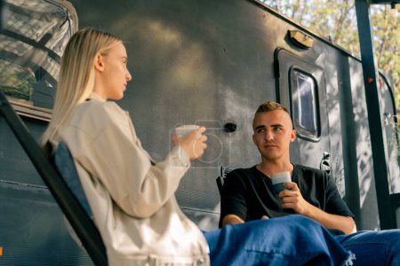 Téléchargez les photos : Un beau mec boit du thé sur la véranda près de la maison mobile et a une conversation fascinante avec sa petite amie - en image libre de droit
