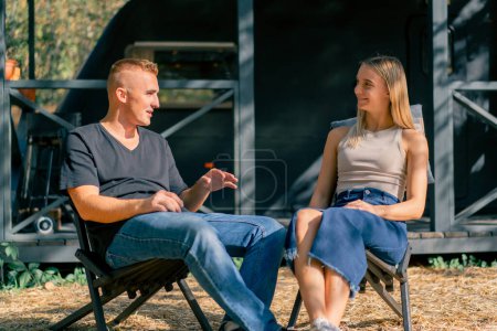 Photo for A young couple a man and a girl are drinking tea on the terrace near their motorhome in a camper - Royalty Free Image