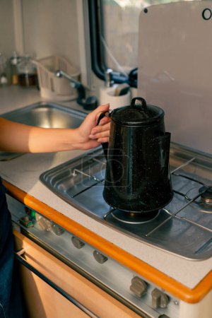 Téléchargez les photos : Gros plan de la main d'une femme mettant une bouilloire sur un poêle à gaz pour chauffer l'eau pour préparer le thé avec de l'eau bouillante - en image libre de droit