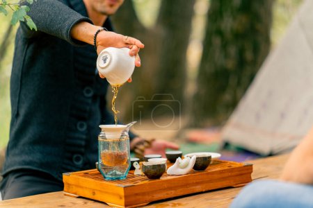 Foto de La mano de un hombre vierte agua hirviendo en tazones de cerámica para hacer té en una clase magistral de ceremonia del té - Imagen libre de derechos