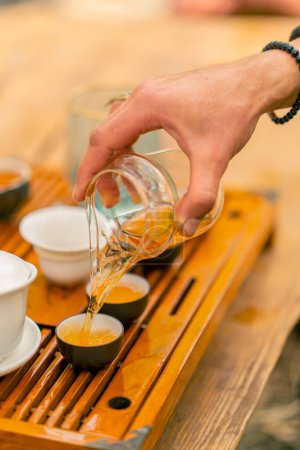 Téléchargez les photos : Gros plan sur le thé chinois naturel infusé versé dans des bols en céramique lors d'une cérémonie traditionnelle du thé - en image libre de droit