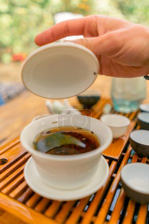 Téléchargez les photos : Gros plan des feuilles de thé chinois naturel brassées dans un bol en céramique spécial avec un couvercle pendant la cérémonie - en image libre de droit