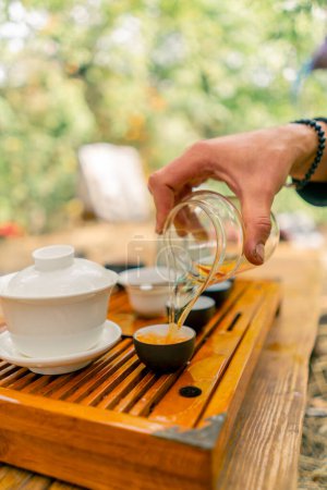 Téléchargez les photos : Gros plan de la main d'un homme versant du thé naturel infusé dans des bols en céramique alignés en rang - en image libre de droit
