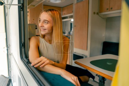 Foto de Una hermosa chica monta en un remolque en un viaje mira por la ventana abierta y sonríe sinceramente desde las hermosas vistas en el camino - Imagen libre de derechos