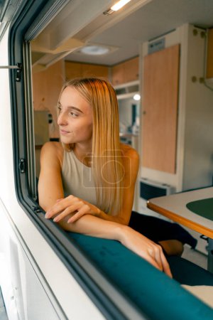 Foto de Una hermosa chica monta en un remolque en un viaje mira por la ventana abierta y sonríe sinceramente desde las hermosas vistas en el camino - Imagen libre de derechos
