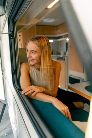 Téléchargez les photos : Une belle fille monte dans une remorque lors d'un voyage regarde par la fenêtre ouverte et sourit sincèrement des belles vues le long du chemin - en image libre de droit