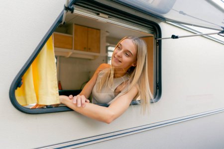 Téléchargez les photos : Une jeune fille regarde par la fenêtre ouverte en montant dans une remorque lors d'un voyage et sourit joyeusement - en image libre de droit