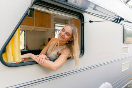 Téléchargez les photos : Une jeune fille regarde par la fenêtre ouverte en montant dans une remorque lors d'un voyage et sourit joyeusement - en image libre de droit