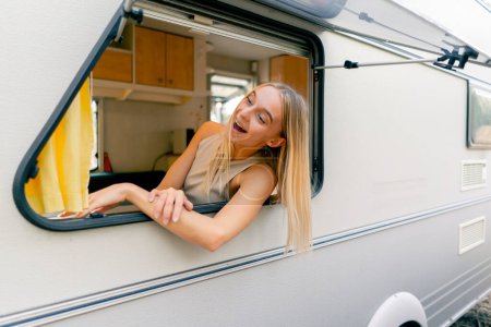 Foto de Una joven mira por una ventana abierta mientras monta en un remolque en un viaje y sonríe alegremente - Imagen libre de derechos