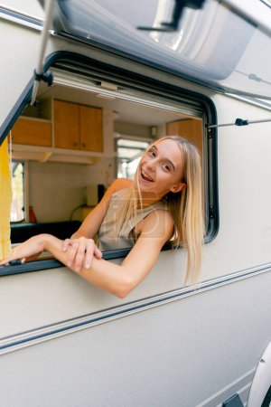 Foto de Una joven mira por una ventana abierta mientras monta en un remolque en un viaje y sonríe alegremente - Imagen libre de derechos