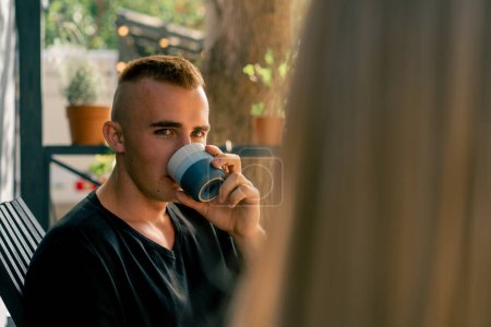 Téléchargez les photos : Gros plan d'un jeune homme assis sur la terrasse près d'un mobil-home buvant du thé et écoutant attentivement sa petite amie - en image libre de droit