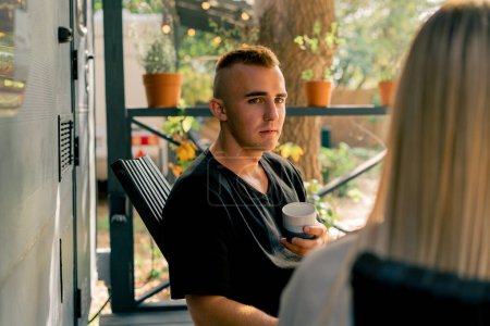 Photo for A handsome guy drinks tea on the veranda near the mobile home and has a fascinating conversation with his girlfriend - Royalty Free Image