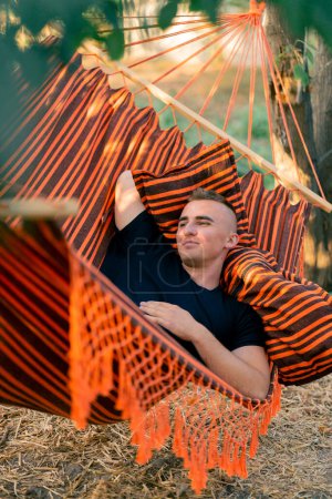 Photo for A guy lies relaxed in a hammock resting and relaxing while vacationing in glamping in the countryside - Royalty Free Image