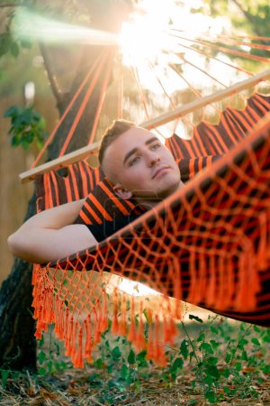 Photo for A guy lies relaxed in a hammock resting and relaxing at sunset while vacationing in glamping in the countryside - Royalty Free Image