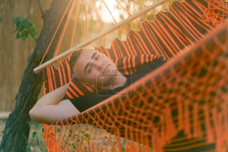 Photo for A guy lies relaxed in a hammock resting and relaxing at sunset while vacationing in glamping in the countryside - Royalty Free Image