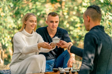 Téléchargez les photos : Un maître de thé professionnel passe un bol de thé couvert d'un couvercle à un jeune couple souriant pour la dégustation - en image libre de droit
