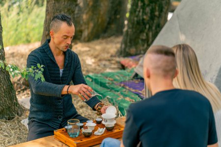 Téléchargez les photos : Un maître de cérémonie du thé masculin inhabituel verse l'eau bouillante d'une théière en verre spéciale lors d'une cérémonie traditionnelle du thé chinois - en image libre de droit