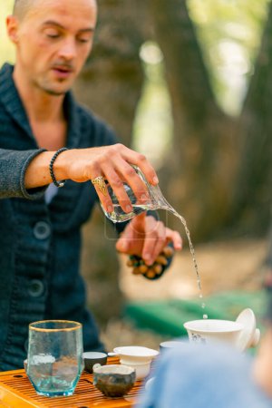 Foto de Un primer plano de un maestro del té usando un kit tradicional de ceremonia del té para verter agua hirviendo de una tetera en una mesa de madera de chaban - Imagen libre de derechos