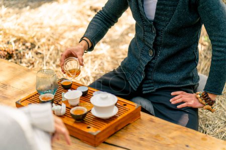 Foto de Las manos de un maestro de té profesional que vierte té verde natural fresco de una tetera de vidrio en cuencos en una mesa de madera chaban - Imagen libre de derechos