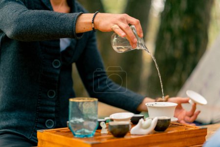 Photo for A man's hand pours boiling water into ceramic bowls for making tea at a tea ceremony masterclass - Royalty Free Image
