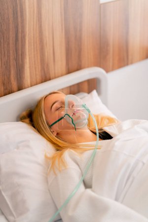 Téléchargez les photos : Gros plan d'une jeune fille allongée en soins intensifs dans un masque à oxygène dans un hôpital pour maintenir la santé et la vie de la patiente - en image libre de droit