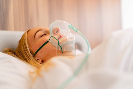 Photo for Close-up shot of a young girl lying in intensive care in an oxygen mask in a hospital to maintain the health and life of the patient - Royalty Free Image