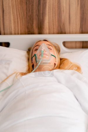 Photo for Close-up shot of a girl lying in hospital room wearing an oxygen mask to a maintain breathing during illness - Royalty Free Image