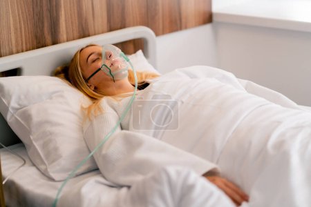 Photo for Close-up shot of a girl lying in hospital room wearing an oxygen mask to a maintain breathing during illness - Royalty Free Image
