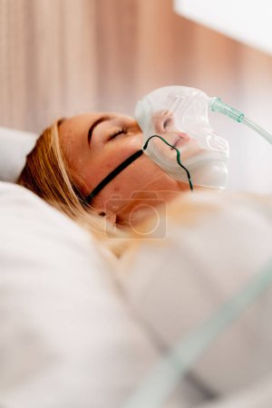Téléchargez les photos : Gros plan d'une fille allongée dans une chambre d'hôpital portant un masque à oxygène pour maintenir sa respiration pendant la maladie - en image libre de droit