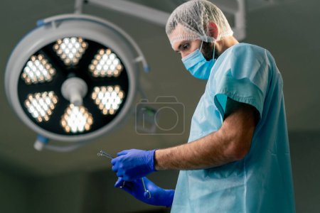 Photo for A doctor in the operating room in a protective uniform and a special headdress puts on gloves before an operation in an operating room - Royalty Free Image