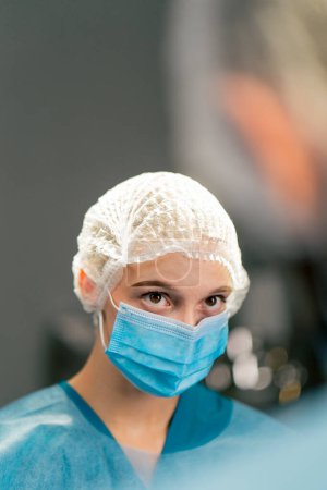 Photo for Close-up shot of a female surgical assistant in uniform and medical mask listening attentively to her colleague during an operation - Royalty Free Image