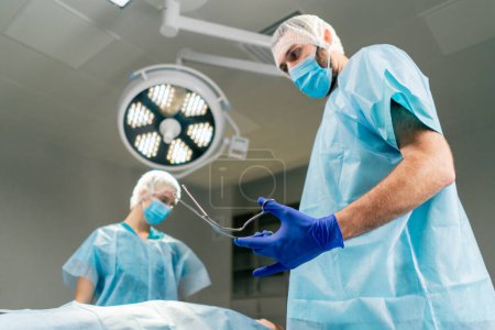 Téléchargez les photos : Le chirurgien prend un scalpel stérilisé au métal pour commencer l'opération dans la salle d'opération. - en image libre de droit