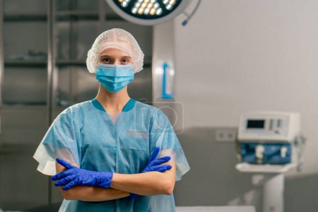 Foto de Retrato de una anestesióloga con uniforme y máscara médica en quirófano con los brazos cruzados delante de ella - Imagen libre de derechos