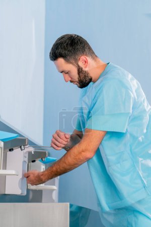 Foto de Un médico de uniforme médico se lava las manos bajo el grifo y las desinfecta con un antiséptico antes del trabajo. - Imagen libre de derechos