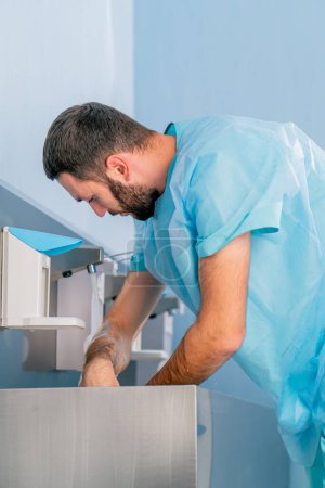 Téléchargez les photos : Un médecin en uniforme médical se lave les mains sous le robinet et les désinfecte avec un antiseptique avant le travail - en image libre de droit