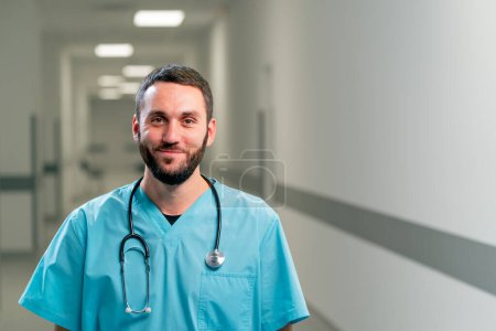 Téléchargez les photos : Portrait d'un médecin souriant avec une barbe et un stéthoscope autour du cou dans le couloir d'un centre médical spacieux - en image libre de droit