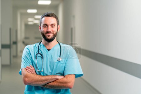 Foto de Retrato de un médico sonriente con barba y un estetoscopio alrededor del cuello en el pasillo de un amplio centro médico - Imagen libre de derechos