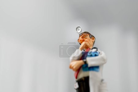 Téléchargez les photos : Gros plan d'une figurine en céramique d'un médecin en manteau blanc avec un réflecteur frontal sur le front - en image libre de droit